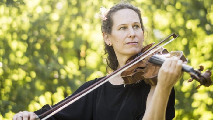 woman plays violin amidst light dappled nature background