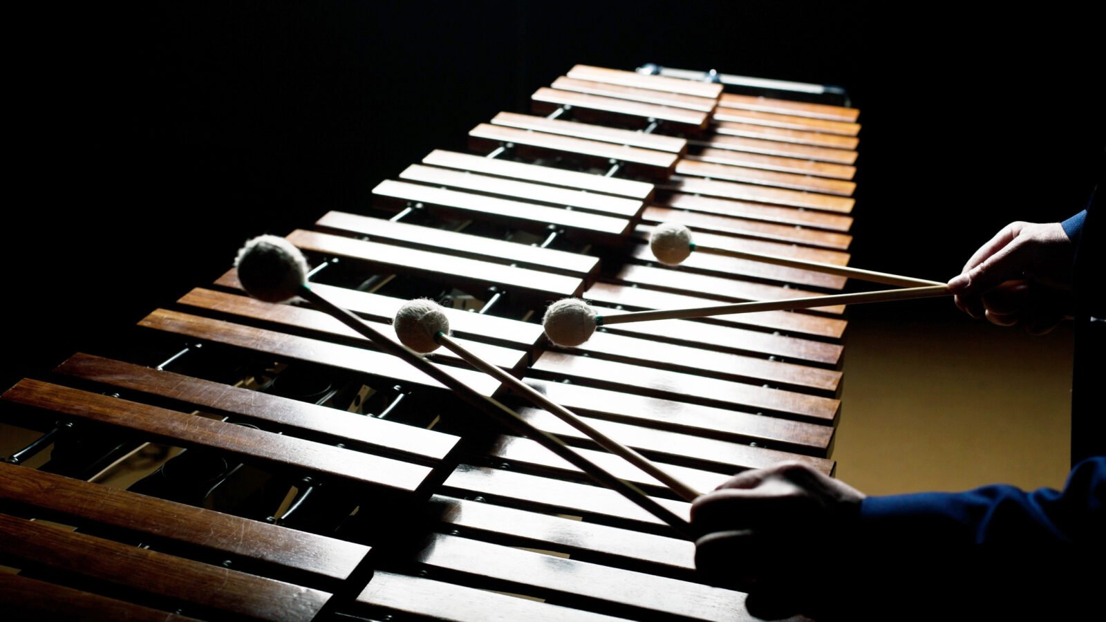 musician holds mallets over xylophone in dark room