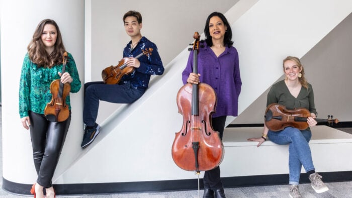 four informally dressed musicians pose casually with their instruments