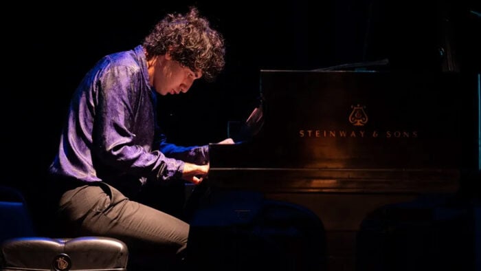 young man in colorful shiny shirt plays the piano with focus