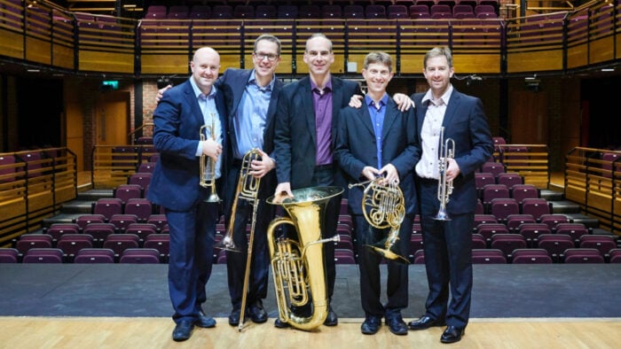 five brass musicians pose onstage