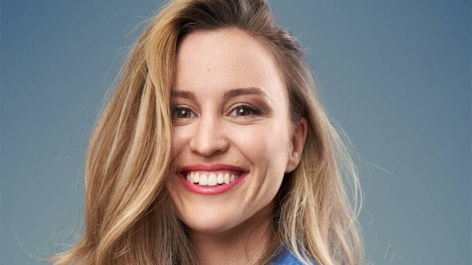 Smiling blonde woman in front of bluish backdrop