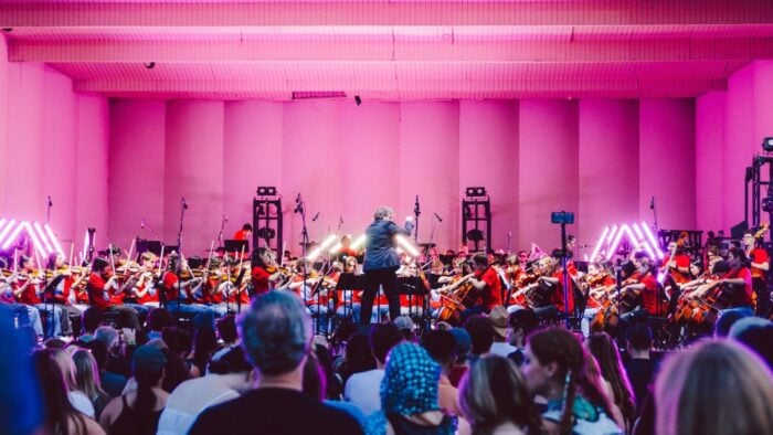 orchestra and conductor on pink-lit stage with audience looking on