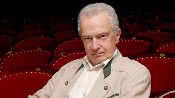 serious looking older man sitting in red velvet theater seats
