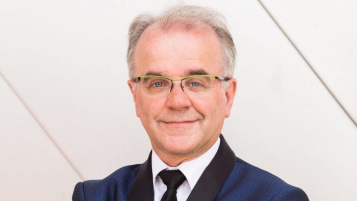 Man in patterned blue dinner jacket , black tie, and vivid yellow glasses poses