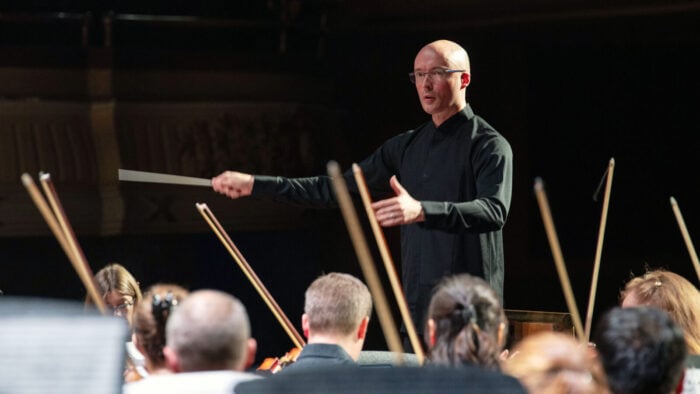 man in dark shirt conducts an orchestra