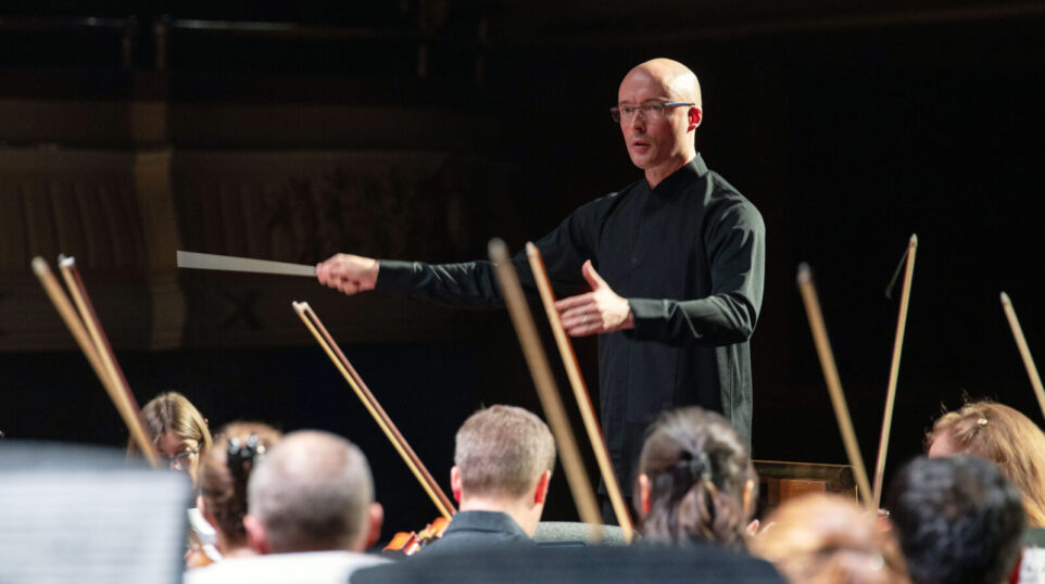man in dark shirt conducts an orchestra