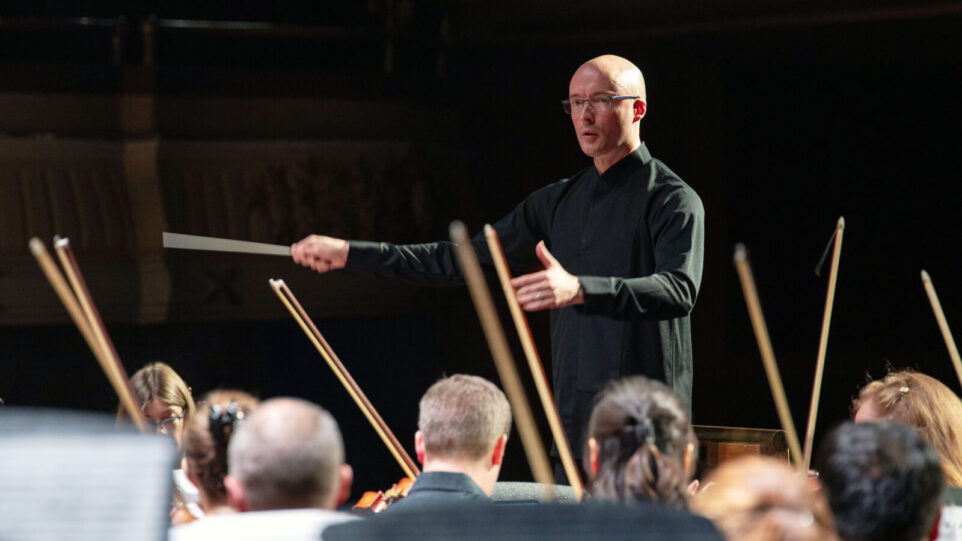 man in dark shirt conducts an orchestra
