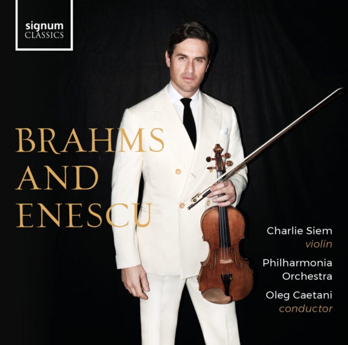 Man in cream suit and black tie holds violin