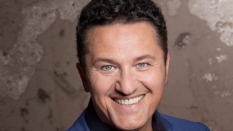 man in blue suit smiles brilliantly in front of weathered wall