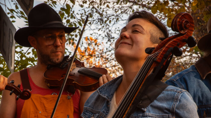 man wearing hat plays fiddle next to woman playing bass