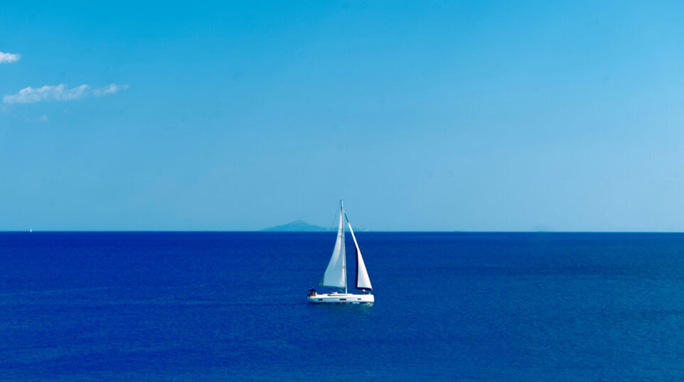 A Sail Boat out at Sea with distant destination in the background