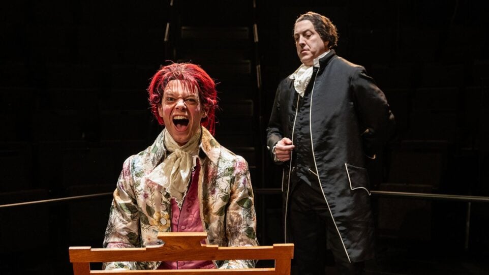 Performance mage from Steppenwolf Theatre's production of "Amadeus." Ian Barford as Salieri, dressed in black looking over the shoulder of David Darrow as Mozart at the fortepiano in an extravagant floral coat, red wig.