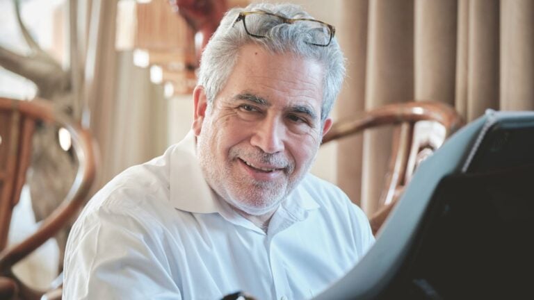 Close up of Carlo Rizzi seated at the piano, white dress shirt, eyeglasses resting on his forehead.