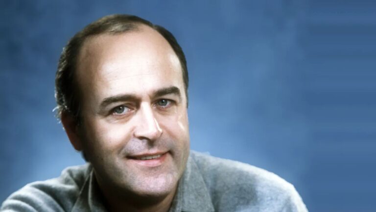 José van Dam portrait in wool grey shirt; blue backdrop; probably photographed in 70s or 80s as he still has natural hair color.