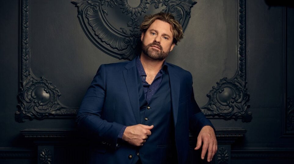 Portrait of Randall Scotting in a navy blue three-piece suit, matching blue shirt, no tie; leaning on a mantle, complicaated moulding and wall also in blue.