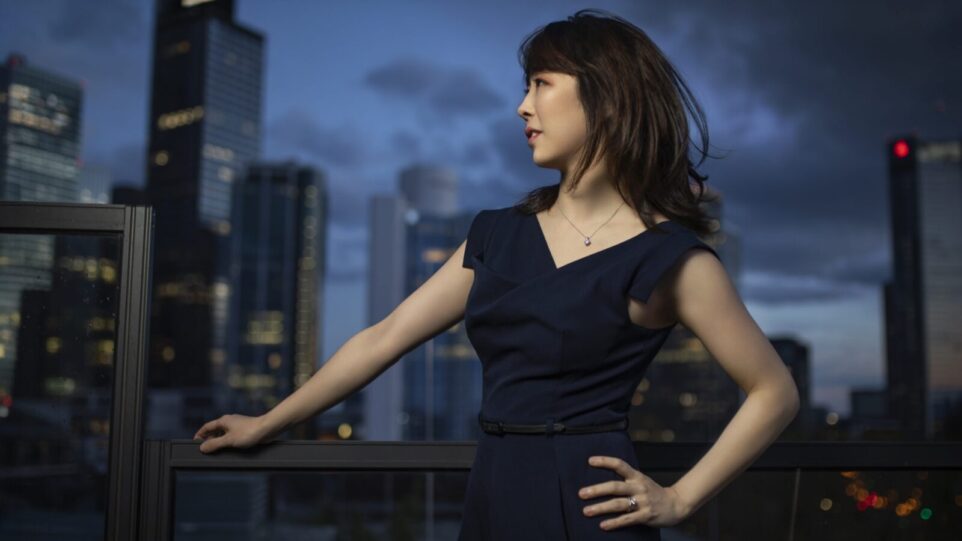 Claire Huangci posing in front of a city skyline and a grey, cloudy sky
