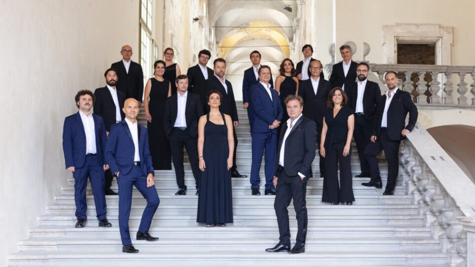 a group of men and women dressed in classical music attire, positioned on various steps on a marble staircase
