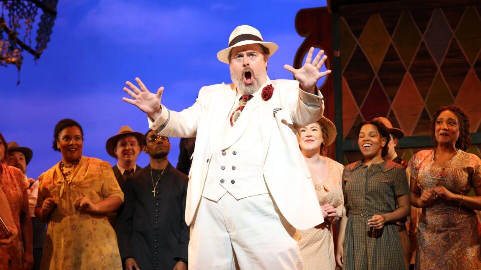 Jonathan Burton as Canio in "Pagliacci" in and all-white three piece suit and fedora; chorus in background.