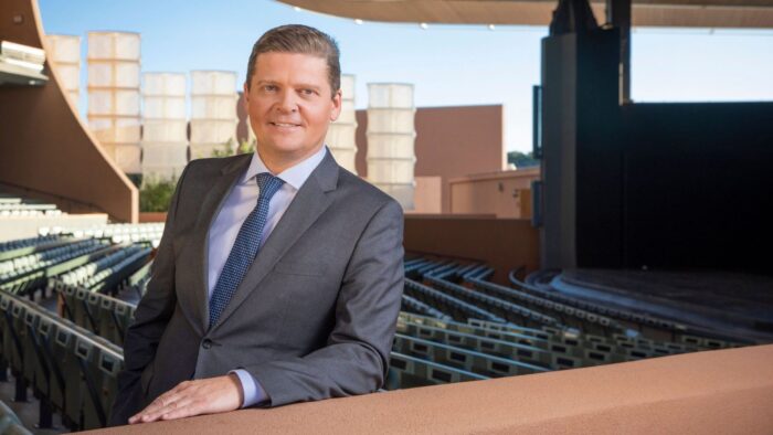 Portrait of Robert K. Meya in a grey suit, posing in the open air Crosby Theatre on a sunny day.