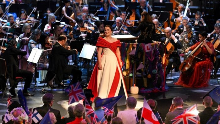 Louise Alder in a Union Kack-inspired gown on the stage of Royal Albert Hall; the BBC Symphony Orchestra and conductor Elim Chan behind her; a large crowd with many holding Union Jack flags in front of her.