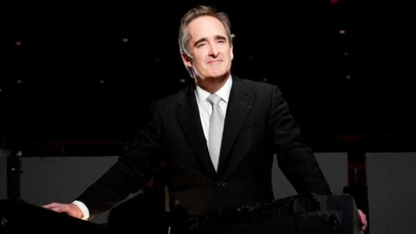 An Interview with James Conlon James Conlon wearing a dark suit, white shirt, light grey tie, posing in the orchestra pit of LA Opera's Dorothy Chandler Pavilion.