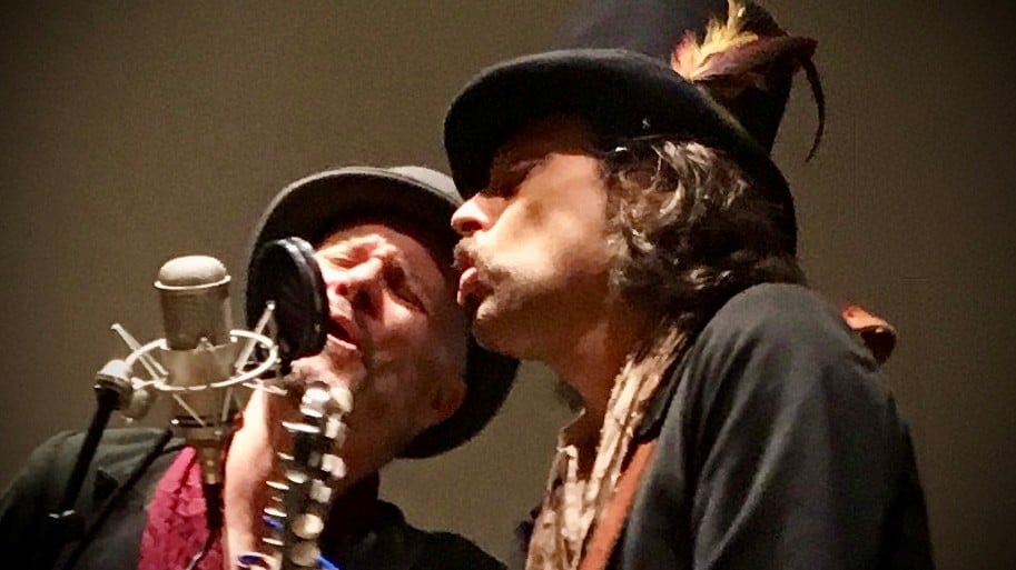 two men in Victorian garb sing into one microphone