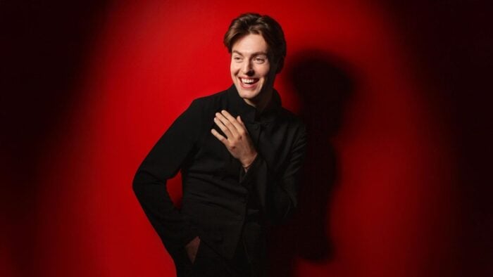 Laurence Kilsby in a dark suit, red backgorund with a lot of shadow creating strong contrast with his fair complexion.