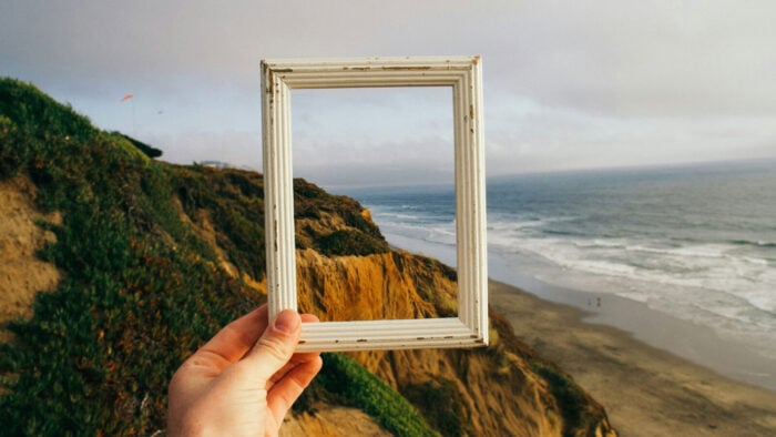 Someone holding up a picture frame on the coast of a large body of water