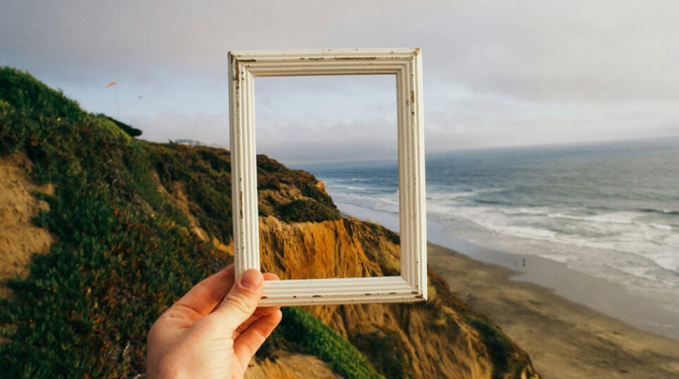 Someone holding up a picture frame on the coast of a large body of water