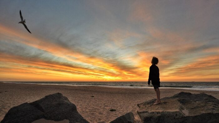 Silhouette of boy looking out to sea at sunset.