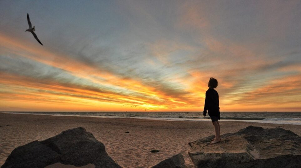 Silhouette of boy looking out to sea at sunset.