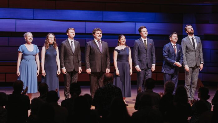 Three ladies and five gentlemen of VOCES8 bowing at a performance, men in suits, women in simple dark gowns.
