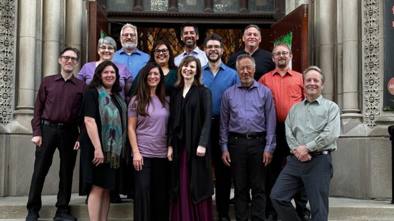 13 musicians (5 women, 8 men) of King Solomon's Singers; men in dark slacks and dress shirts of various solid colors; wome in a combination of blouse/pants or simple dresses all in solid colors, posing in front of the doors of St Josephat Church in Lincoln Park.