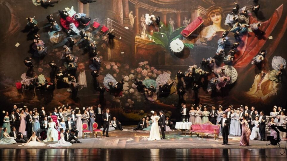 A staging of a ballroom of people, with a giant ballroom scene painting in the background.
