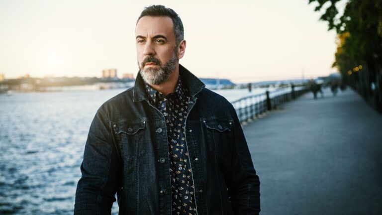 Portrait of Christian Van Horn in denim jacket taken outdoors taken at sunset or early morning at a boardwalk, water and sidewalk in background.