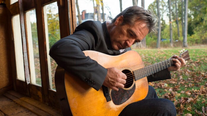 seated man leans over as he plays his guitar