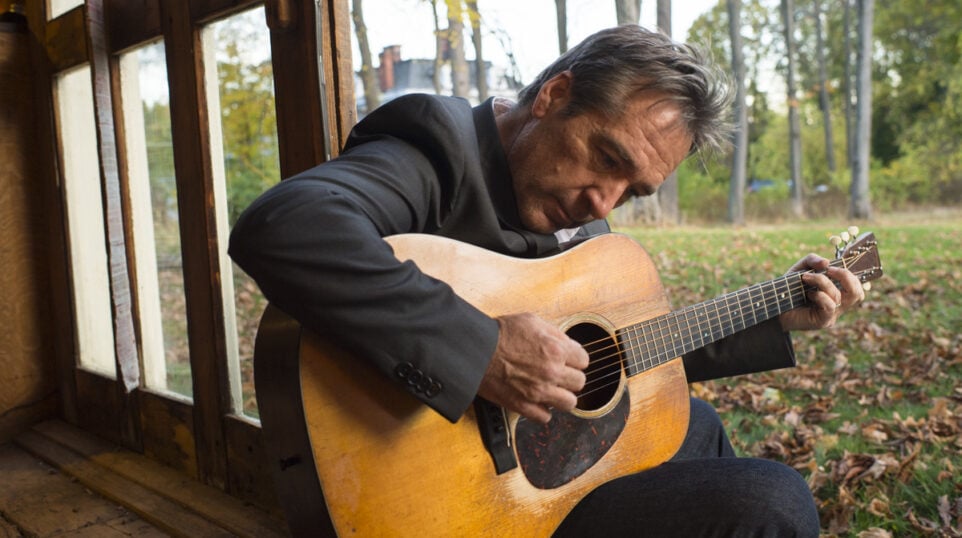 seated man leans over as he plays his guitar