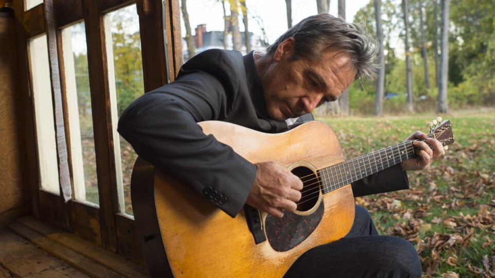 seated man leans over as he plays his guitar