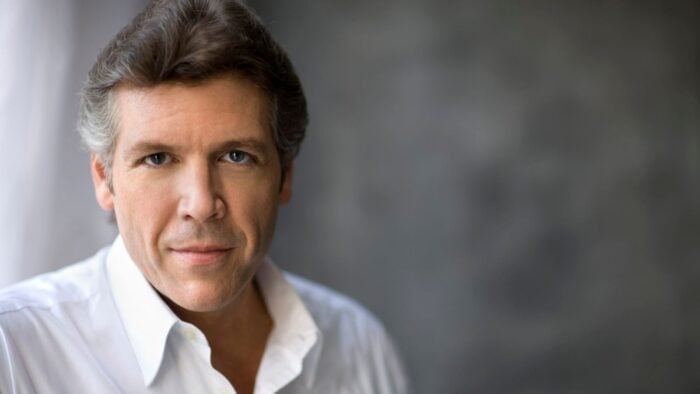 Thomas Hampson in open collar white dress shirt, looking directly into camera, composition mostly in left side of frame, soft focus, grey back drop.