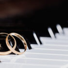 a pair of gold wedding bands rest together on the keys of a piano