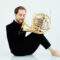 Felix Klieser, dressed in black, holds his French horn with his feet